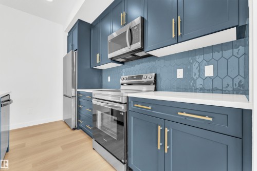 The kitchen features blue cabinetry with gold-toned hardware, white countertops, and a blue hexagonal tile backsplash - 57 710 Mattson Drive, Edmonton, AB - Indoor Photo Showing Kitchen