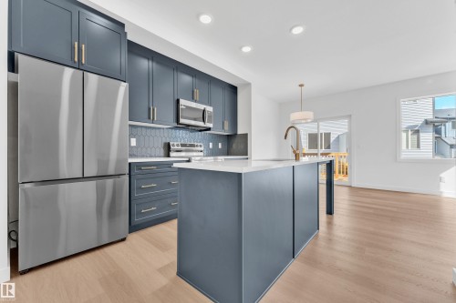 The kitchen features dark blue cabinetry with gold hardware, stainless steel appliances, and a white countertop on the island - 57 710 Mattson Drive, Edmonton, AB - Indoor Photo Showing Kitchen With Upgraded Kitchen