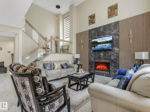 This living space features high ceilings, a contemporary fireplace, and a striking accent wall with vertical wood paneling and marble-style tiling - 1147 Lincoln Crescent, Edmonton, AB - Indoor Photo Showing Living Room With Fireplace