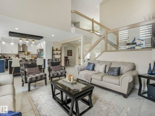 The property features an open-concept living area with high ceilings, a modern kitchen with a large island and pendant lighting, and a contemporary glass and wood staircase - 1147 Lincoln Crescent, Edmonton, AB - Indoor Photo Showing Living Room