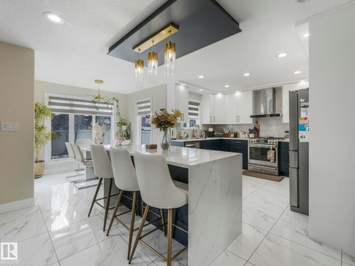 This property features a kitchen and dining area with white tiled flooring, a kitchen island with a white countertop and seating, and a modern light fixture - 1147 Lincoln Crescent, Edmonton, AB - Indoor