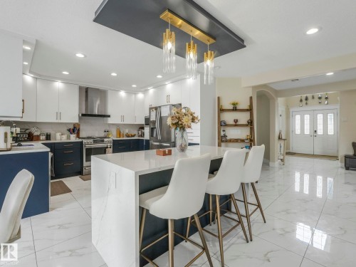 The kitchen features an island with a light-colored countertop and seating, white upper cabinetry, and dark lower cabinetry - 1147 Lincoln Crescent, Edmonton, AB - Indoor