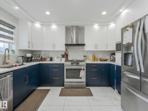 The kitchen features white upper cabinetry, blue lower cabinetry, and stainless steel appliances including a refrigerator, range, and dishwasher - 1147 Lincoln Crescent, Edmonton, AB - Indoor Photo Showing Kitchen With Double Sink With Upgraded Kitchen