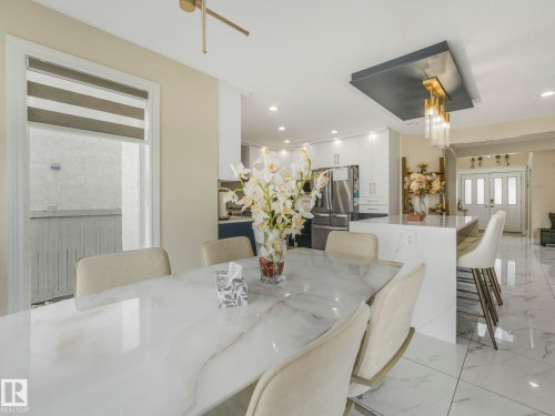 The open concept dining area features a large table with a polished surface, upholstered chairs, and tiled flooring - 1147 Lincoln Crescent, Edmonton, AB - Indoor Photo Showing Dining Room