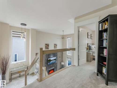 An interior view of the property, featuring a staircase with a glass and wood railing, light-colored carpeting, and a window with horizontal blinds - 1147 Lincoln Crescent, Edmonton, AB - Indoor Photo Showing Other Room