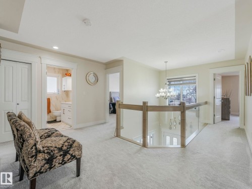 The property features light-colored carpeting throughout, a staircase with a glass and wood railing, and a window providing views to the outside - 1147 Lincoln Crescent, Edmonton, AB - Indoor Photo Showing Other Room