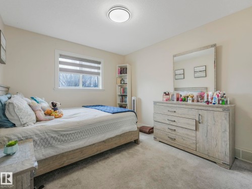 This room features light-colored carpeting and walls, a window with horizontal blinds, and a built-in bookshelf - 1147 Lincoln Crescent, Edmonton, AB - Indoor Photo Showing Bedroom