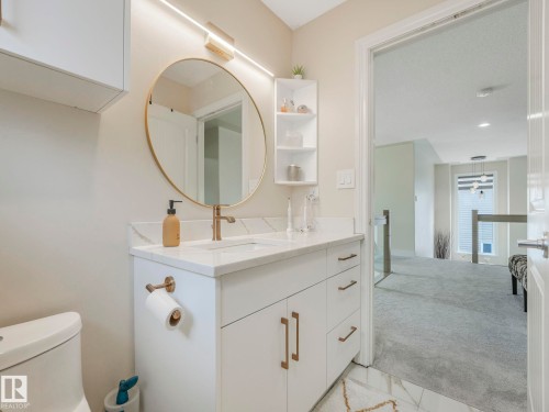 The bathroom features a vanity with a white countertop and sink, a round gold-framed mirror, and a linear light fixture above - 1147 Lincoln Crescent, Edmonton, AB - Indoor Photo Showing Bathroom