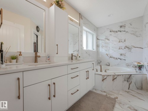 Bathroom featuring a double vanity with white cabinetry and bronze hardware, a built-in bathtub, and marble-patterned tile flooring and walls - 1147 Lincoln Crescent, Edmonton, AB - Indoor Photo Showing Bathroom