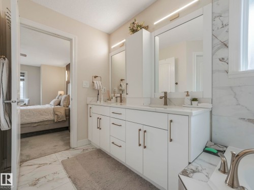 Bathroom featuring a double vanity with white cabinetry and bronze hardware, marble-look countertops, and a large mirror with integrated lighting - 1147 Lincoln Crescent, Edmonton, AB - Indoor Photo Showing Bathroom