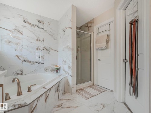 The bathroom features an elegant bathtub, a glass-enclosed shower, and walls and flooring adorned with marble-patterned tiles - 1147 Lincoln Crescent, Edmonton, AB - Indoor Photo Showing Bathroom