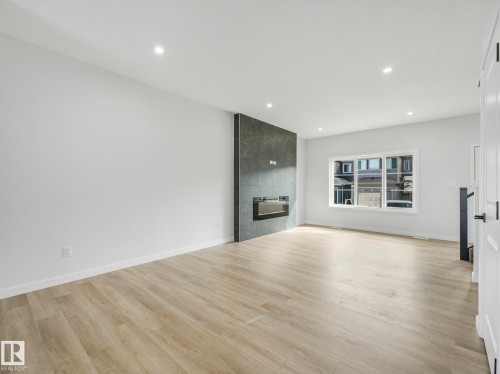 Spacious living area featuring light-toned flooring, a modern electric fireplace with a dark tile surround, and recessed lighting - 275 Munn Way, Leduc, AB - Indoor With Fireplace