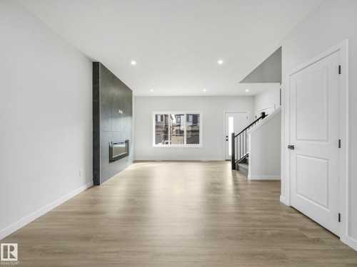 The property features an open-concept living space with light-toned flooring, recessed lighting, and a modern fireplace with a dark-tiled surround - 275 Munn Way, Leduc, AB - Indoor With Fireplace