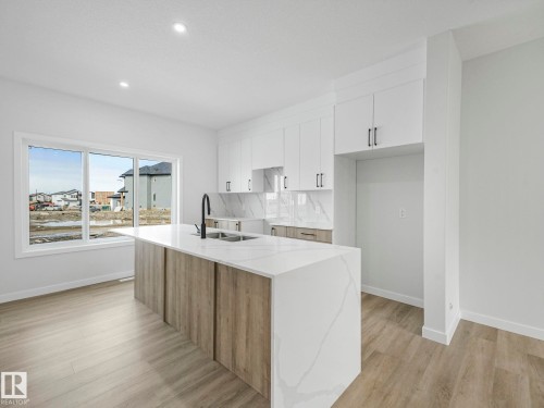 Contemporary kitchen featuring a spacious island with a waterfall countertop, white cabinetry with black hardware, and wood-look flooring - 275 Munn Way, Leduc, AB - Indoor Photo Showing Kitchen With Double Sink