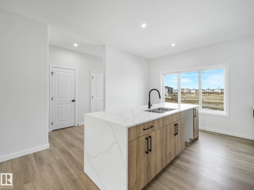 The kitchen features a spacious island with a white countertop and natural wood cabinetry, complemented by a contemporary black faucet and double sink - 275 Munn Way, Leduc, AB - Indoor Photo Showing Kitchen With Double Sink