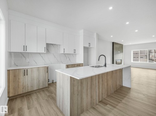 The kitchen features a large island with a sink and modern faucet, white upper cabinets, and wood-look lower cabinets - 275 Munn Way, Leduc, AB - Indoor Photo Showing Kitchen With Upgraded Kitchen