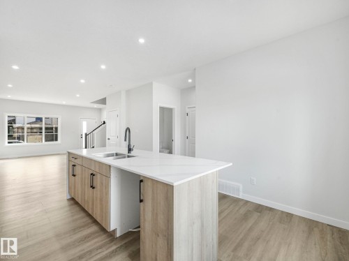 Open concept kitchen and living area featuring a kitchen island with an undermount sink, light wood cabinetry, and a light-colored countertop - 275 Munn Way, Leduc, AB - Indoor Photo Showing Kitchen With Double Sink