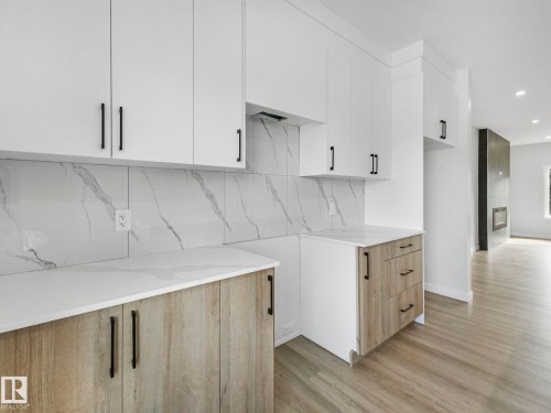 The kitchen features white upper cabinetry, light wood-toned lower cabinetry, white countertops, and a white backsplash with gray veining - 275 Munn Way, Leduc, AB - Indoor