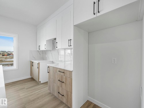 Modern kitchen featuring white upper cabinetry, wood-look lower cabinetry, and white countertops with a marble-style backsplash - 275 Munn Way, Leduc, AB - Indoor