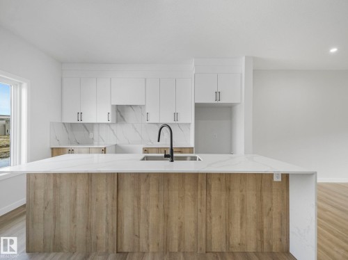 Modern kitchen featuring a large island with a light-colored countertop and a matte black faucet - 275 Munn Way, Leduc, AB - Indoor Photo Showing Kitchen