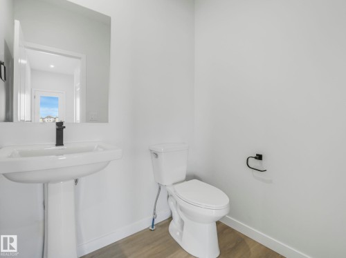 This powder room features a pedestal sink with a modern black faucet, a toilet, and light-toned flooring - 275 Munn Way, Leduc, AB - Indoor Photo Showing Bathroom