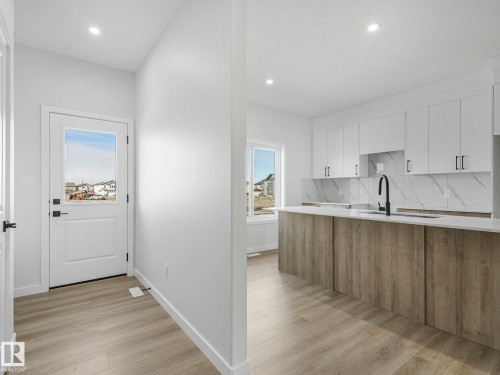 This property features a bright and spacious kitchen with white cabinetry, a large island with a wood-grain finish, and a modern black faucet - 275 Munn Way, Leduc, AB - Indoor
