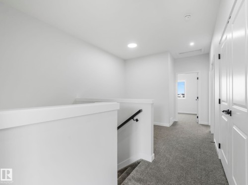 The property features a staircase with a black handrail and a white half-wall, leading to a hallway with grey carpeting - 275 Munn Way, Leduc, AB - Indoor Photo Showing Other Room
