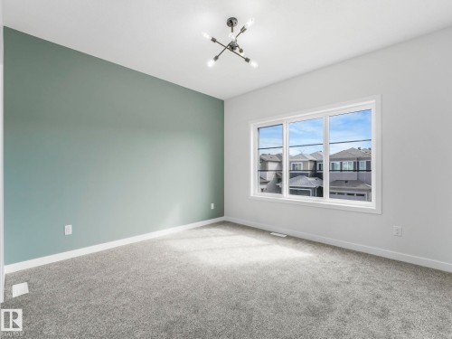 This room features a contemporary light fixture, a window providing natural light, and plush grey carpet - 275 Munn Way, Leduc, AB - Indoor Photo Showing Other Room