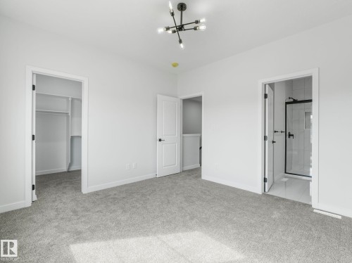 Spacious room featuring light gray carpeting, crisp white walls, and a contemporary black chandelier - 275 Munn Way, Leduc, AB - Indoor Photo Showing Other Room