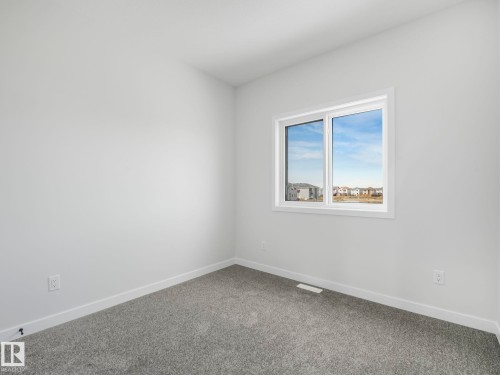 The property features light gray carpeting and white walls, complemented by a window with a white frame - 275 Munn Way, Leduc, AB - Indoor Photo Showing Other Room