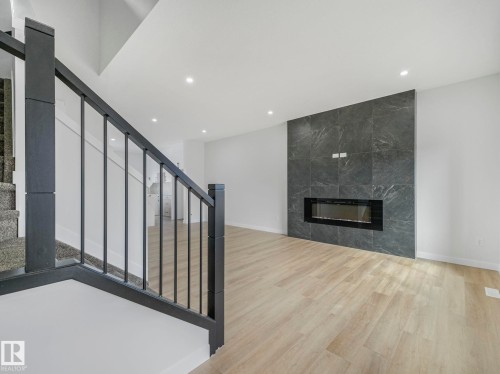The living area features light-toned flooring, a sleek fireplace set into a dark tile wall, and recessed lighting in the ceiling - 275 Munn Way, Leduc, AB - Indoor With Fireplace