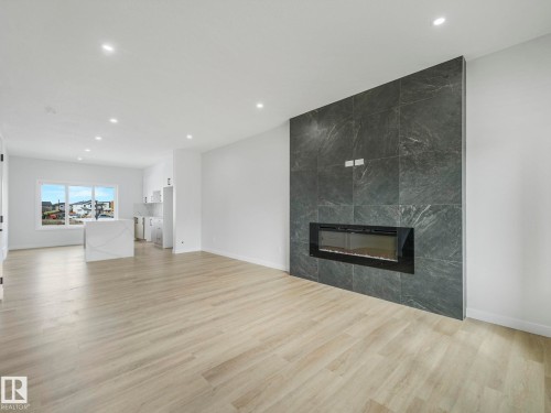 Spacious open-concept living area featuring light-toned flooring, recessed lighting, and a modern fireplace integrated into a dark tiled accent wall - 275 Munn Way, Leduc, AB - Indoor Photo Showing Living Room With Fireplace