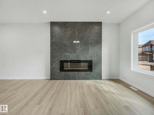 Spacious room with light-toned flooring, a large window, recessed lighting, and a modern fireplace with a dark tiled surround - 275 Munn Way, Leduc, AB - Indoor Photo Showing Living Room With Fireplace