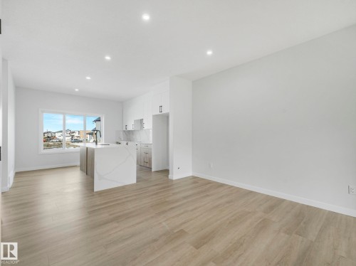 The open concept living area features light-toned flooring, recessed lighting, and a kitchen with a waterfall island, a sink with a black faucet, and white cabinetry - 275 Munn Way, Leduc, AB - Indoor