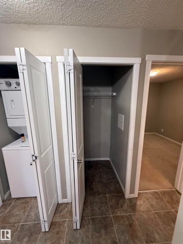 This area features tiled flooring, a built-in closet with shelving, and a stacked washer and dryer - 104 3207 James Mowatt Trail, Edmonton, AB - Indoor Photo Showing Laundry Room