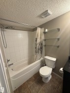 Bathroom featuring a white bathtub with white tiled walls, a white toilet, and brown tiled flooring - 
