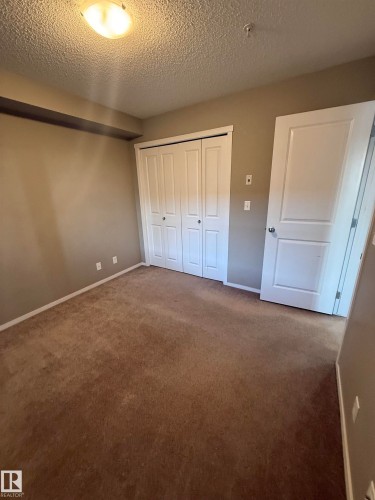 This room features a brown carpeted floor, light taupe walls, and a white bi-fold closet door - 104 3207 James Mowatt Trail, Edmonton, AB - Indoor Photo Showing Other Room