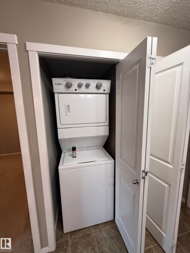Convenient laundry closet with a stacked washer and dryer, featuring white bi-fold doors and tile flooring - 104 3207 James Mowatt Trail, Edmonton, AB - Indoor Photo Showing Laundry Room