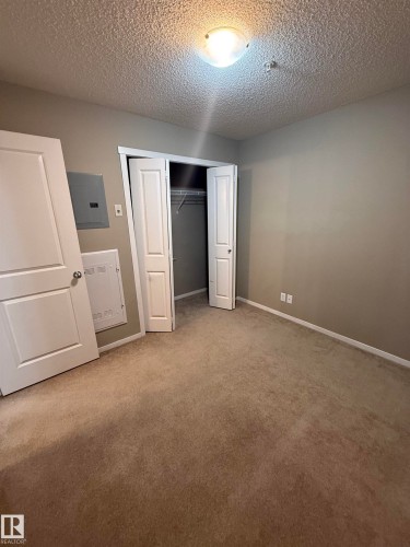 This room features soft carpeting, a closet with bi-fold doors, and a ceiling-mounted light fixture - 104 3207 James Mowatt Trail, Edmonton, AB - Indoor