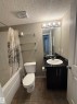 The bathroom features a bathtub with a shower, a toilet, and a vanity with a sink, black countertop, and dark cabinetry - 104 3207 James Mowatt Trail, Edmonton, AB  - Indoor Photo Showing Bathroom 