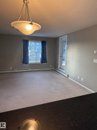 Living area featuring light-colored carpeting, a window with blinds and blue curtains, and a door leading outside - 