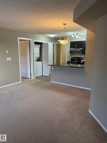 This property features a kitchen with dark cabinetry, integrated stove, and a double basin sink - 104 3207 James Mowatt Trail, Edmonton, AB - Indoor Photo Showing Other Room