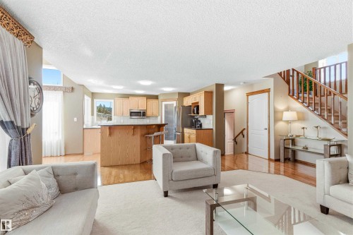 The property features an open-concept living area with hardwood flooring, a kitchen with light wood cabinetry and stainless steel appliances, and a staircase with wooden railings - 442 Hunters Green, Edmonton, AB - Indoor Photo Showing Living Room