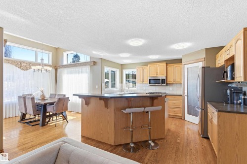 Open concept kitchen and dining space featuring hardwood floors, light wood cabinetry, a central island with a dark countertop, and large windows providing natural illumination - 442 Hunters Green, Edmonton, AB - Indoor Photo Showing Kitchen