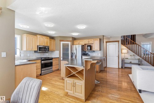 The property features a kitchen with wood cabinetry, stainless steel appliances, and a central island with a built-in wine rack - 442 Hunters Green, Edmonton, AB - Indoor Photo Showing Kitchen