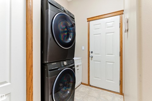 Laundry area featuring a stacked washer and dryer, tiled flooring, and a white paneled door with wood trim - 442 Hunters Green, Edmonton, AB - Indoor Photo Showing Laundry Room
