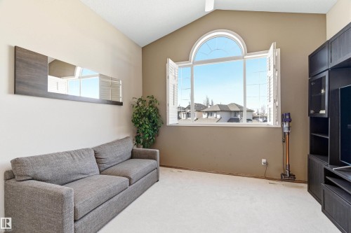 The property features a spacious room with a vaulted ceiling, a large arch-top window with white shutters, and light-colored carpeting - 442 Hunters Green, Edmonton, AB - Indoor Photo Showing Other Room