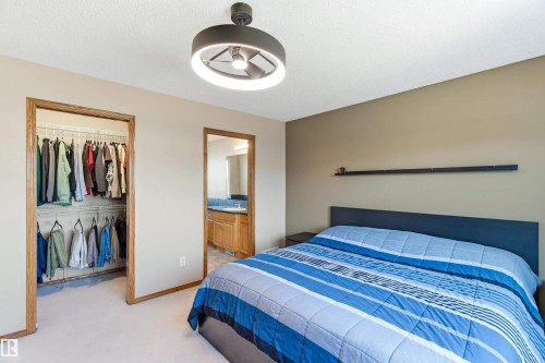 This bedroom features a modern ceiling fan with integrated lighting, a spacious closet with built-in shelving, and an entryway to an adjoining bathroom - 442 Hunters Green, Edmonton, AB - Indoor Photo Showing Bedroom