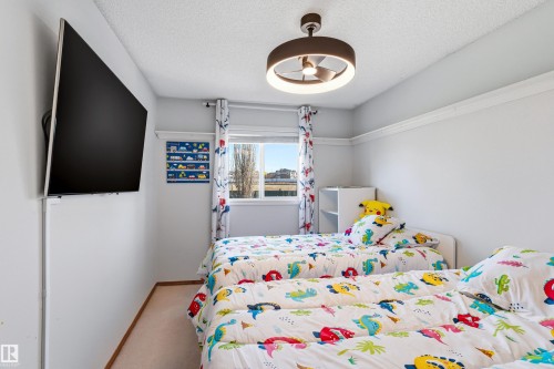 Bedroom with a ceiling-mounted light fixture, window with curtains, and a wall-mounted display - 442 Hunters Green, Edmonton, AB - Indoor Photo Showing Bedroom