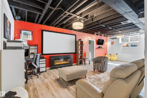 This versatile space features light-toned flooring, an exposed ceiling with track lighting, and a large projection screen above an electric fireplace - 442 Hunters Green, Edmonton, AB - Indoor Photo Showing Basement With Fireplace